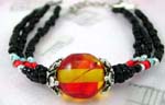 Unique beaded jewelry supplied by international wholesaler. Bracelet with three small black beaded strings each holding a silver, red, and blue bead that come together with orange and yellow glass bead in center between two silver decorated stones.