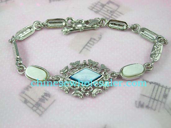 Fashion jewelry bracelet supplied wholesale from importinga agent. Light blue, diamond shaped center with  fancy design around connected by seashell inlaid in oval shaped chains. Toggle clasp for closure.    
              
        