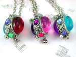 Costume jewelry distributed online from wholesale manufacturing company. Silver plated chian holds double backed colored gemstones set in oval shaped pendant frame with four smaller stones embedded in and two bells dangling below.